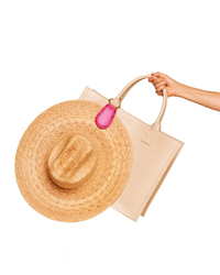 A person's hand holding a straw hat with a TopTote hat holder and a beige tote bag featuring high-powered magnet closure against a white background.