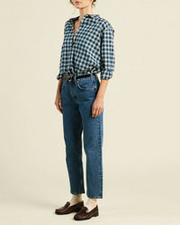 Someone wears the Trovata Birds of Paradis Blake Oversized Shirt in Maritime Plaid, tucked into high-waisted blue jeans with a black belt, beige socks, and brown loafers, standing against a plain background.