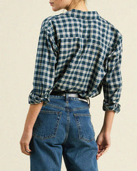 A person is shown from the back wearing the Trovata Birds of Paradis Blake Oversized Shirt in Maritime Plaid with rolled-up sleeves, paired with high-waisted blue jeans against a plain, neutral background.