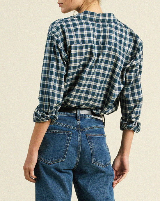 A person is shown from the back wearing the Trovata Birds of Paradis Blake Oversized Shirt in Maritime Plaid with rolled-up sleeves, paired with high-waisted blue jeans against a plain, neutral background.