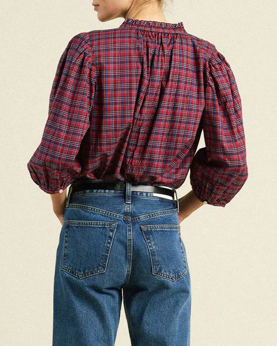 A person wearing the Trovata Birds of Paradis Orly Blouse in Mulled Wine Plaid with puffed sleeves paired with blue denim jeans, seen from behind. The blouse is tucked in and cinched with a black belt.