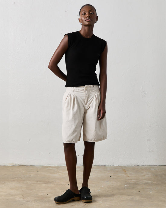 Person stands against a plain white wall wearing a black sleeveless top, NSF Quinn Culotte in Soft White, and black shoes.