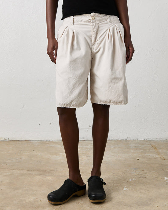A person wearing urban chic, light-colored Quinn Culotte in Soft White by NSF and black clogs, standing on a concrete floor in front of a white wall.