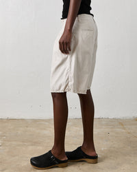 A person wearing the NSF Quinn Culotte in Soft White, a black top, and black clogs stands on a concrete floor against a plain white wall, embodying an urban chic style.
