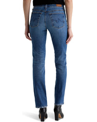 A person is shown from the back wearing AG Jeans’ Sandra Low Rise Straight in 15Ys Prague—a medium blue wash jean with two back pockets and a brown waistband patch, styled with black heeled boots, hands at their sides.