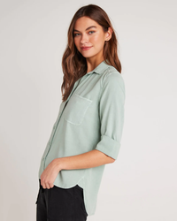 Woman posing in a light green Bella Dahl Shirt Tail Button Down in Oasis Green with a collar and rolled-up sleeves.