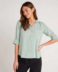 Woman smiling and posing in a casual mint green Bella Dahl Shirt Tail Button Down in Oasis Green TENCEL™ Lyocell button-down shirt and black trousers.