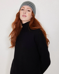 Woman with red hair wearing a black turtleneck and a Not Monday Tate Cashmere Beanie in Storm Grey & Jade Stripe.