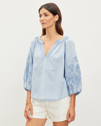 Woman posing in a Velvet by Graham & Spencer Trina L/S Boho Top in Chambray and white shorts against a plain background.