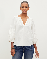 A woman wearing a Velvet by Graham & Spencer Trina L/S Boho Top in Off White and blue jeans standing against a plain background.