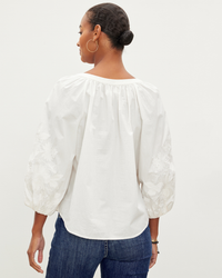 Woman in a Trina L/S Boho Top in Off White by Velvet by Graham & Spencer with embroidered sleeves and blue jeans, viewed from behind.