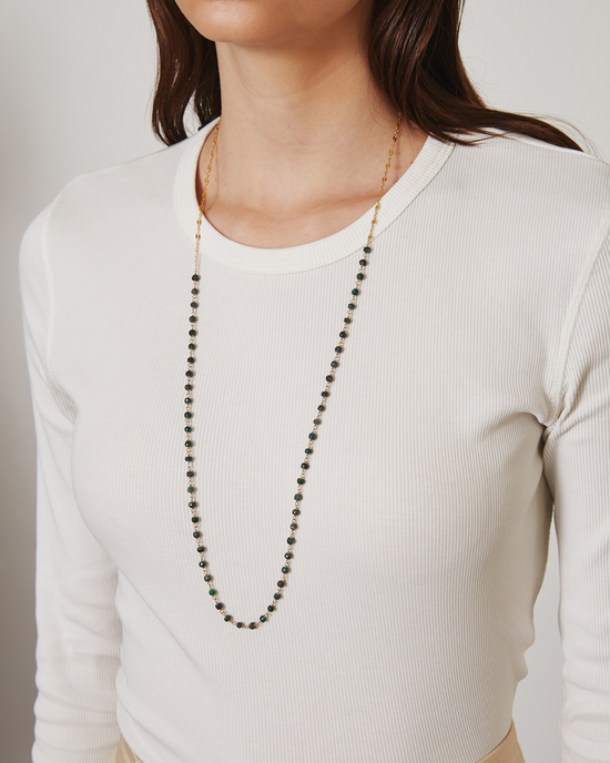 Woman in a white ribbed top wearing a long Chan Luu emerald beads necklace (CL NG-14732), focusing on the torso area with a neutral background.