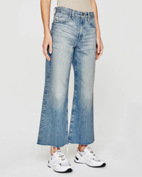 Person wearing frayed, AG Jeans Saige Wide Leg Crop in Rival bell-bottom jeans and white sneakers.