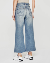A person wearing AG Jeans' Saige Wide Leg Crop in Rival with frayed hems and white sneakers.