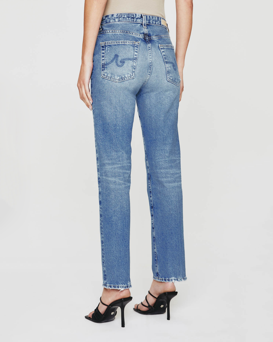 A person standing in AG Jeans Saige High Rise Straight in 16Ys Cupola blue high waisted straight leg pants and black high-heeled shoes with a medium indigo wash.