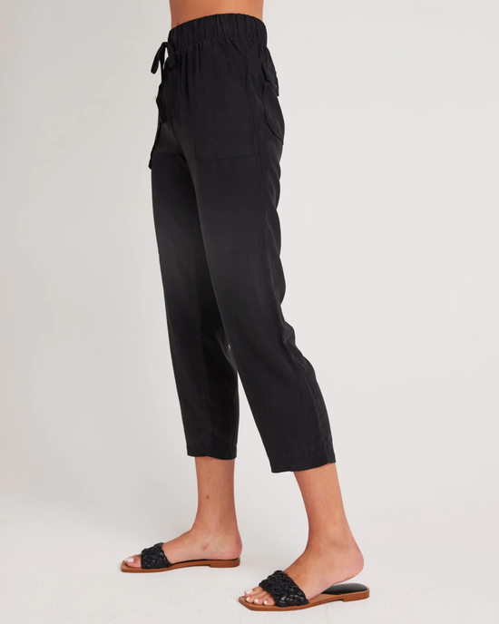 A person standing side-on wearing Bella Dahl's Utility Tie Waist Trouser in Vintage Black and black slide sandals.