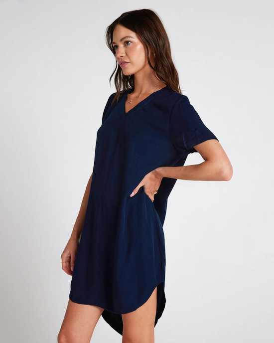 A woman poses in a plain navy V-Neck Dress in Endless Sea by Bella Dahl with her hand on her hip against a neutral background.