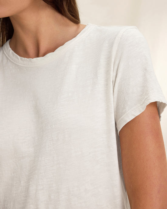A close-up of a person wearing the Marika Short Sleeve Crew Neck Crop Top in White by Velvet by Graham & Spencer, highlighting their neck, shoulder, and arm against a neutral background.