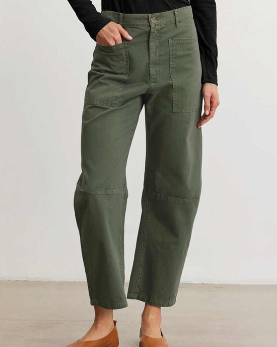 Someone stands against a plain light background wearing Velvet by Graham & Spencer's Brylie Curved Knee Pant in Caper, featuring front patch pockets, paired with a black long-sleeve top and brown flats.
