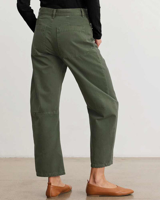 A person wearing Velvet by Graham & Spencer’s Brylie Curved Knee Pant in Caper and tan flats stands indoors on a light floor, facing away to show the casual trouser’s large back pockets.