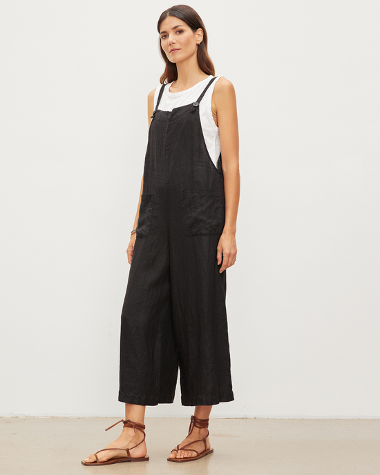 A woman posing in a Velvet by Graham & Spencer Isabel Jumpsuit in Black and a white t-shirt, paired with strappy sandals.