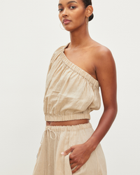 A woman in a Laleen One Shoulder Crop Top in Biscuit by Velvet by Graham & Spencer and matching drawstring pants posing against a white background.