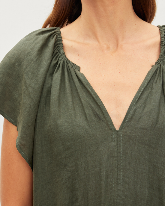 Close-up of a person wearing a green linen Pepper S/S Drawstring Dress in Tootise by Velvet by Graham & Spencer with gathered sleeves and a v-neckline featuring coastal-inspired styling.