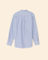 The XiRENA Beau Shirt in True Blue, a 100% cotton oversized button-down with blue and white vertical stripes, collar, buttoned cuffs, and a back pleat, is shown from the back on a beige background.