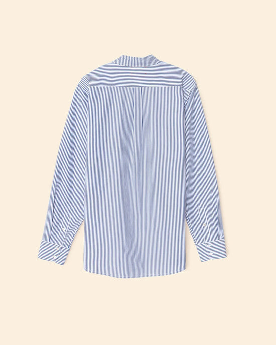 The XiRENA Beau Shirt in True Blue, a 100% cotton oversized button-down with blue and white vertical stripes, collar, buttoned cuffs, and a back pleat, is shown from the back on a beige background.