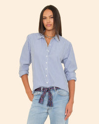 A woman with straight, dark hair wears an oversized XiRENA Beau Shirt in True Blue, featuring blue and white stripes, styled with light jeans, a colorful belt, and layered necklaces against a neutral background.