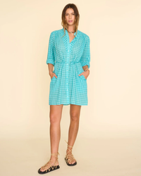 Woman in a Winnie Dress in Aqua Blue by XiRENA and lace-up sandals posing against a beige background.
