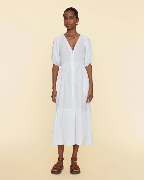 A woman wearing a white cotton gauze XiRENA Lennox Dress in White with brown strappy sandals stands against a neutral background.