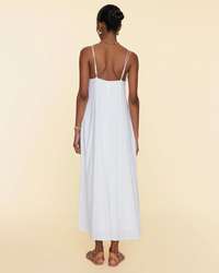 A woman stands with her back to the camera, wearing a XiRENA Teague Dress in White with thin straps and sandals, against a neutral background.