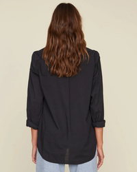 Woman seen from behind wearing a XiRENA Black Beau Shirt, made of Cotton Poplin, with rolled-up sleeves and blue jeans.