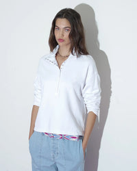 Young woman in a XiRENA McCoy Sweatshirt in White and blue jeans standing against a light-colored background.