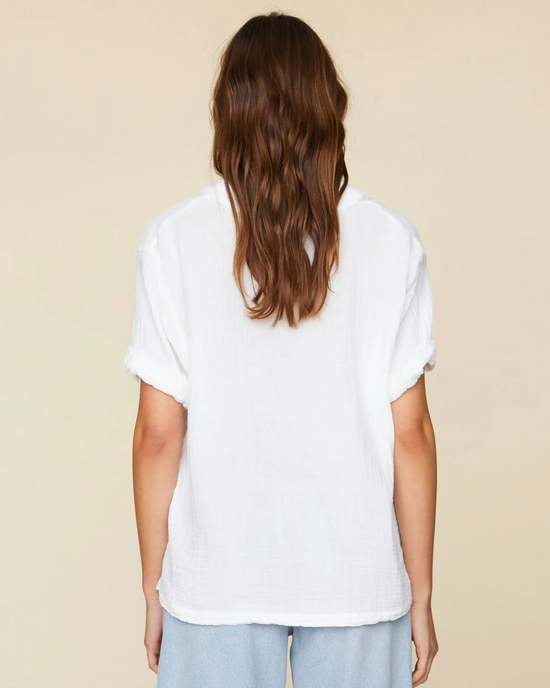 Woman standing with her back to the camera, wearing a XiRENA Avery Top in White and blue jeans.