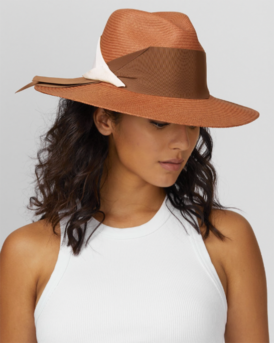 A woman in a white tank top wearing a wide-brimmed brown hat with a white grosgrain band by Freya Gardenia in Clay/Bone.