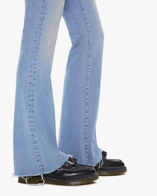 Person wearing The Weekender Fray in Califorina Cruiser jeans by Mother with frayed hem and black shoes with frayed laces standing against a white background.