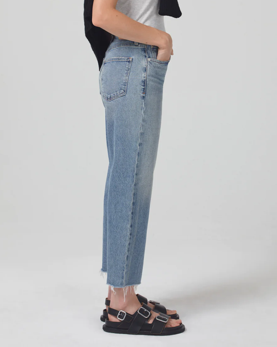Woman standing sideways wearing Citizens of Humanity Florence Wide Straight jeans in Totem with a cropped raw hem and black sandals.