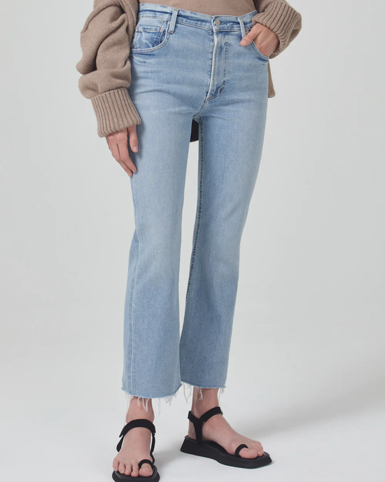 Light blue Citizens of Humanity Isola Zip in Lyric jeans paired with black sandals and a brown sweater, against a neutral background.