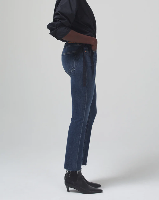 Profile view of a person modeling Citizens of Humanity Isola Cropped Boot in Zip Fly Undercurrent bootcut jeans and black boots on a neutral background.