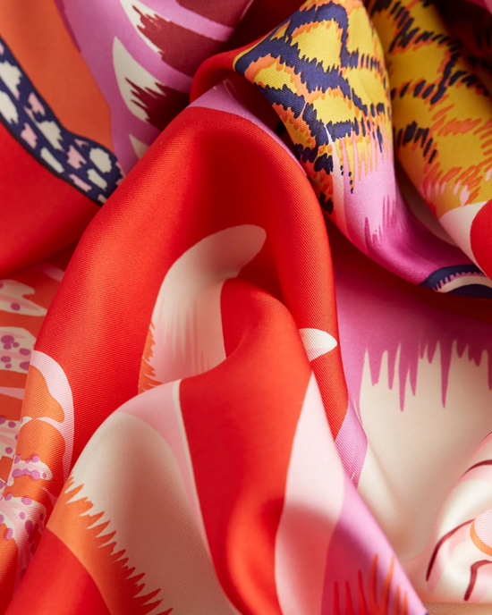 Vibrant, colorful silk fabric with abstract patterns folded elegantly into an oversized Inoui Editions Square 65 Toucan scarf in Red.