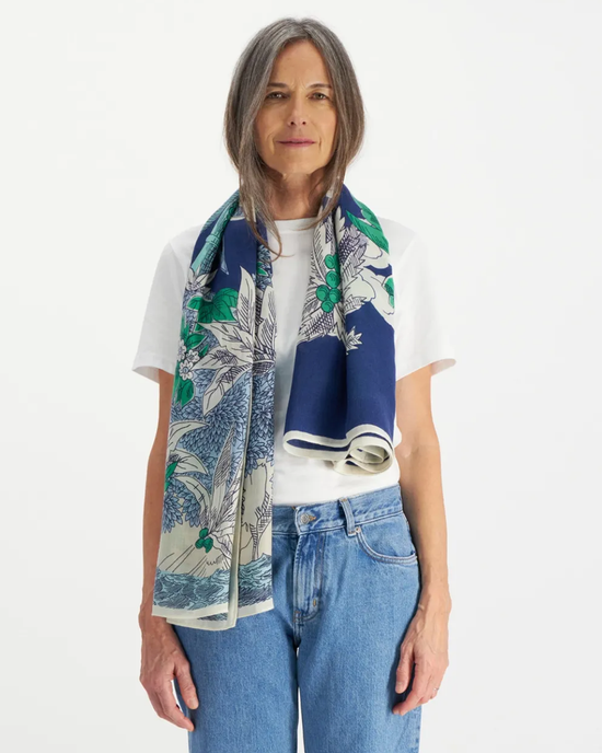 A woman wearing a white t-shirt, blue jeans, and an oversized bandana stands against a white background while holding the Square 130 Robinson in Navy by Inoui Editions.