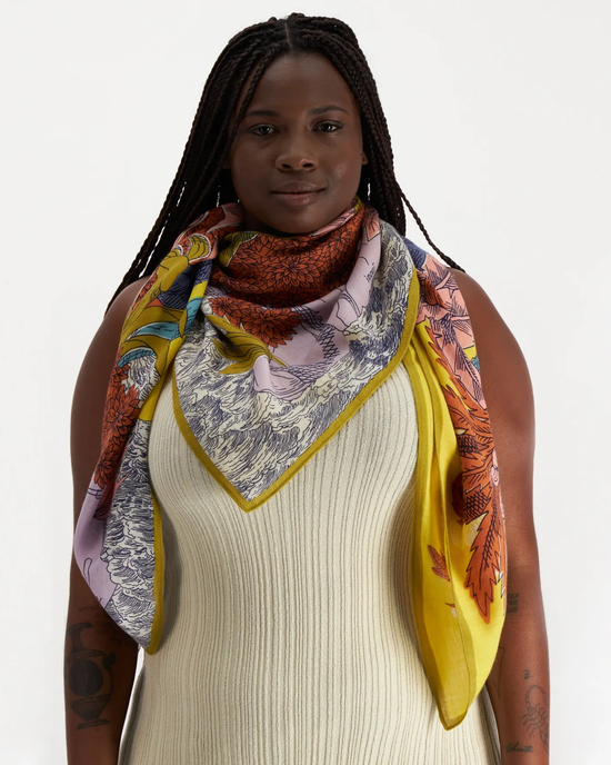 Woman wearing a cream-colored top and an Inoui Editions Square 130 Robinson in Yellow, colorful printed, oversized bandana.