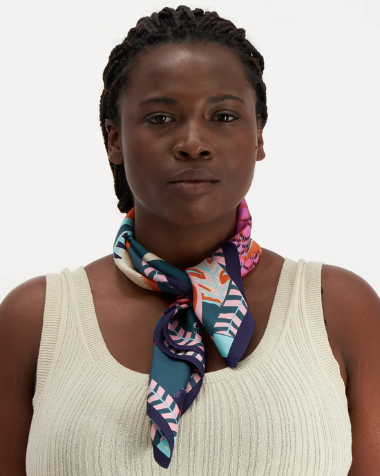 A woman wearing a beige top and an oversized Inoui Editions silk scarf tied around her neck.