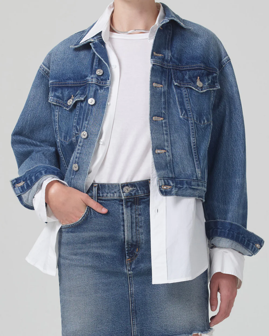 Person wearing a layered outfit with a Citizens of Humanity Dulce Denim Jacket in Brevity and jeans, with a white shirt under the jacket.