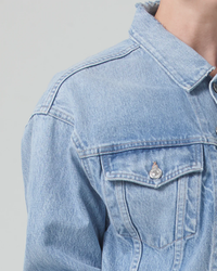 Close-up of a person wearing a Seaplane Dulce Denim Jacket by Citizens of Humanity with a button on the chest pocket.