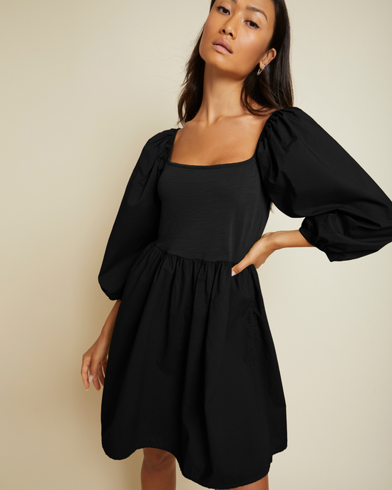 A woman in a black Nation LTD Heddie Combo Babydoll dress with puffy sleeves posing against a neutral background.