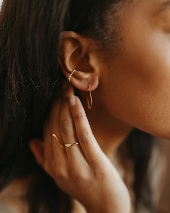 A close-up of a woman's ear showcasing a handmade Box Slide Earring in 14K Gold Fill by Token Jewelry, with her hand touching her ear, adorned with a slender ring.