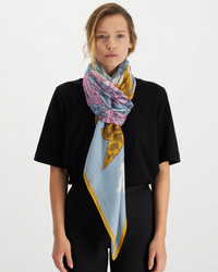 A woman wearing a black top with an oversized Inoui Editions Square 130 Robinson in Blue silk cashmere blend bandana tied around her neck.